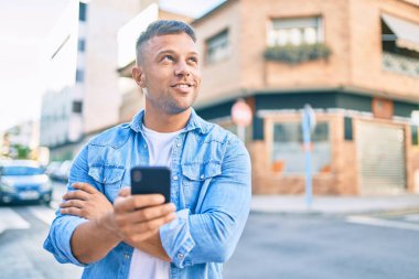 Beyaz adam şehirde akıllı telefon kullanarak mutlu bir şekilde gülümsüyor..