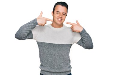 Kış süveteri giyen yakışıklı genç adam neşeli gülüyor ve parmaklarıyla ve ağzıyla işaret ediyor. diş sağlığı kavramı. 