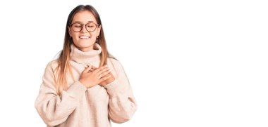 Güzel beyaz kadın yün kazak giyiyor, elleri göğsünde, gözleri kapalı gülümsüyor ve yüzünde minnet ifadesi var. sağlık kavramı. 