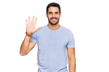 Gündelik kıyafetler giyen genç İspanyol adam beş numarayı gösterip işaret ederken kendinden emin ve mutlu bir şekilde gülümsüyor.. 