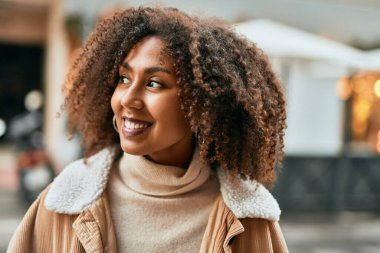Genç Afrikalı Amerikalı kadın gülümseyerek şehirde mutlu mesut duruyor..