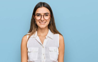 Gündelik kıyafetler giyen genç İspanyol kadın pozitif ve mutlu görünüyor. Dişlerini gösteren kendine güvenen bir gülümsemeyle ayakta ve gülümsüyor. 