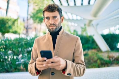 Zarif ceketli yakışıklı bir iş adamı. Açık havada akıllı telefon kullanıyor.