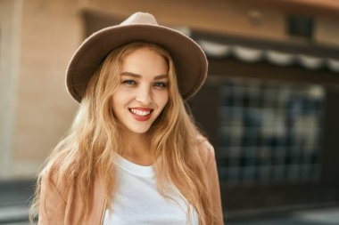 Genç sarışın kız gülümsüyor, mutlu bir şekilde şehirde duruyor..