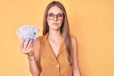 Kolombiya pezosu tutan genç sarışın kız. Düşünce tarzı ve ayık yüz ifadesi. Kendinden emin görünüyor. 