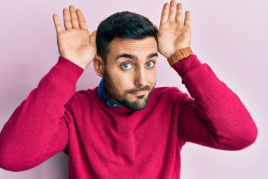 Gündelik kıyafetler giyen, tavşan kulağı yapan, avuçlarıyla alaycı ve şüpheci görünen genç İspanyol bir adam. Paskalya tavşanı konsepti. 