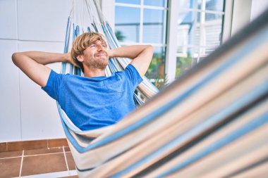 Orta yaşlı yakışıklı bir adam evinin terasında hamakta dinleniyor.