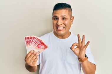 Genç Latin adam elinde 20 İsrail şekeri banknotları tutuyor. Parmaklarıyla imza atıyor, gülümsüyor. Mükemmel bir sembol. 