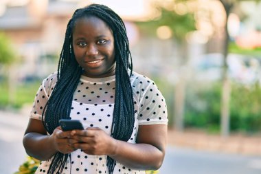 Genç Afrikalı Amerikalı kadın şehirde akıllı telefon kullanarak mutlu bir şekilde gülümsüyor..