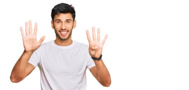 Gündelik beyaz tişört giyen genç yakışıklı dokuz numaralı parmaklarıyla gülümseyerek kendinden emin ve mutlu bir şekilde onu işaret ediyor.. 