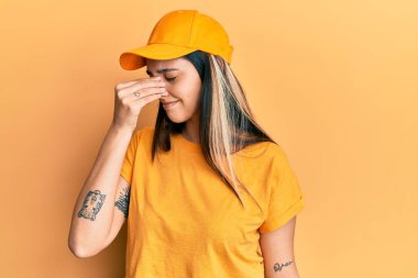 Teslimat üniforması giyen, şapkalı, burnu ve gözleri ovuşturmaktan yorgun düşmüş genç İspanyol kadın yorgunluk ve baş ağrısı hissediyor. Stres ve hüsran kavramı. 