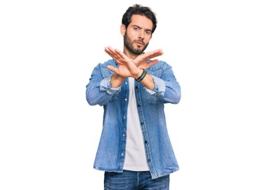 Gündelik kıyafetler giyen genç İspanyol adam. Reddedilmiş yüz ifadesi. Kollarını kavuşturup negatif işaret veriyor. 