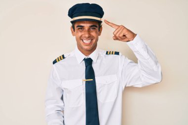 Uçak pilotu üniforması giyen genç İspanyol bir adam gülümseyerek tek parmağıyla kafasını işaret ediyor, harika bir fikir ya da düşünce, iyi bir hafıza. 