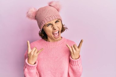 Şirin yün şapkalı genç esmer kadın çılgın bir ifadeyle bağırıyor elleri havada rock sembolü yapıyor. Müzik yıldızı. ağır kavram. 