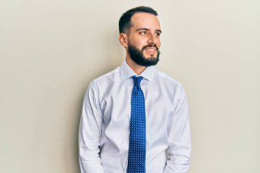 Sakallı, iş kravatlı, yüzünde gülümsemeyle yan yana bakan genç bir adam, doğal bir ifade. Kendinden emin gülen. 