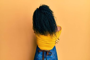 Middle age african american woman wearing professional apron hugging oneself happy and positive from backwards. self love and self care 