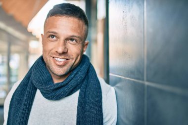 Beyaz bir adam gülümsüyor. Şehrin duvarına yaslanıyor..