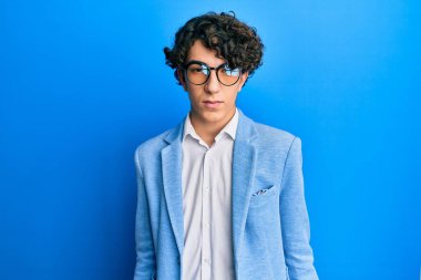 Hispanic young man wearing business jacket and glasses with serious expression on face. simple and natural looking at the camera. 