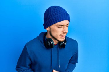 İspanyol genç adam eşofman üstü ve kulaklık takıyor ve elleri karnında çünkü mide bulantısı, acı verici bir hastalık kendini iyi hissetmiyor. Ağrı kavramı. 