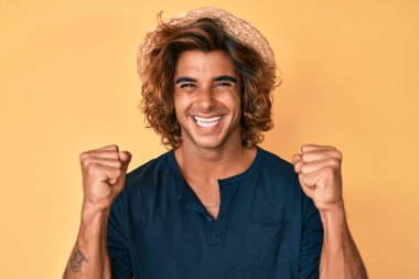 Yaz şapkası takan İspanyol genç adam şaşkınlık ve şaşkınlık içinde kollarını kaldırarak ve gözlerini açarak başarıyı kutluyor. Kazanan konsept. 