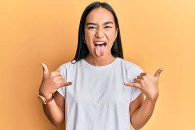 Genç Asyalı kadın Shaka işareti yapıyor. Elleri havada, dili dışarı çıkıyor. Komik bir ifadeyle mutlu.. 