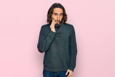 Günlük kıyafetler giyen genç İspanyol adam diş ağrısı ya da diş hastalığından dolayı acı dolu bir ifadeyle ağıza dokunuyor. dişçi 