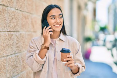 Genç Latin kız akıllı telefondan konuşuyor ve şehirde kahve içiyor..