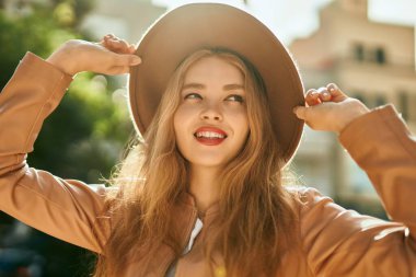 Genç sarışın kız gülümsüyor, mutlu bir şekilde şehirde duruyor..