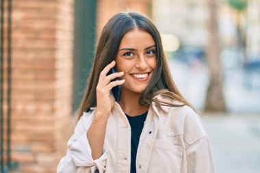 Genç İspanyol kız gülümsüyor. Şehirdeki akıllı telefondan konuşuyor..