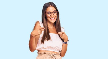 Gündelik kıyafetler giyen ve gözlüklü genç İspanyol kadın mutlu ve komik yüzlü parmaklarını kameraya doğrultuyor. iyi enerji ve titreşimler. 