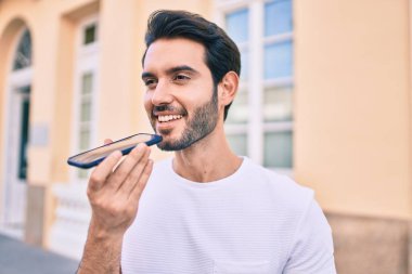 Genç İspanyol adam gülümsüyor. Şehirdeki akıllı telefonu kullanarak sesli mesaj gönderiyor..