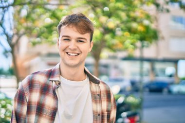 Genç beyaz adam gülümseyerek şehirde mutlu mesut duruyor..