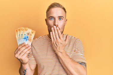 Elinde İsviçre frangı banknotları tutan genç beyaz bir adam ağzını eliyle kapatıyor, şaşırmış ve hata yapmaktan korkuyor. şaşırmış ifade 