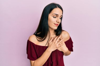 Gündelik kıyafetler giyen genç İspanyol kadın elleri göğsünde, gözleri kapalı ve yüzünde minnet dolu bir jest ile gülümsüyor. sağlık kavramı. 