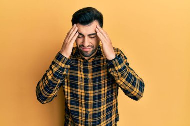 Latin asıllı genç bir adam elleri kafasında günlük kıyafetler giyiyor, stres yüzünden baş ağrısı çekiyor. migren ağrısı. 