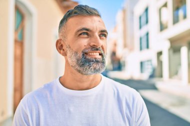 Orta yaşlı, kır saçlı, gülümseyen bir adam şehirde mutlu bir şekilde duruyor..