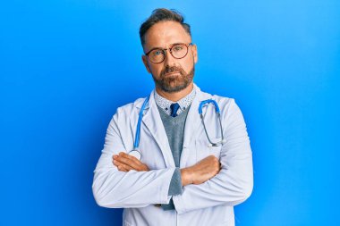 Yakışıklı, doktor üniforması giyen, steteskop kuşkucu ve gergin, yüzünde çapraz kollu tasvip etmeyen orta yaşlı adam. negatif kişi. 