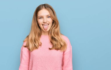 Güzel, genç, beyaz bir kız kışlık süveter giyiyor ve komik bir ifadeyle dilini dışarı çıkarıyor. duygu kavramı. 