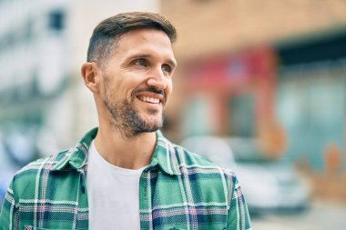 Genç beyaz adam gülümseyerek şehirde mutlu mesut duruyor..