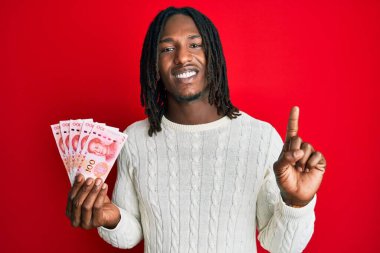 Elinde 100 Yuan 'lık Çin banknotlarıyla gülümseyen ve gülümseyen Afrika kökenli Amerikalı bir adam. 