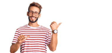 Sarışın, sakallı, sıradan kıyafetler giyen ve gözlüklü, eli ve başparmakları havada, kendinden emin bir şekilde arkasını gösteren yakışıklı bir adam. 