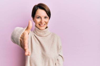 Kısa saçlı, kısa saçlı, kışlık süveter giyen genç esmer kadın dostça bir selamlama ve hoş geldin hediyesi olarak gülümsüyor. başarılı iş. 