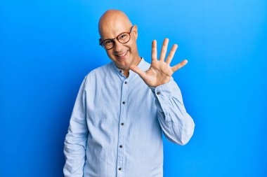 Orta yaşlı, kel, günlük kıyafetler giyen, gözlüklü, beş numaralı parmaklarıyla işaret eden, kendinden emin ve mutlu gülümseyen bir adam.. 