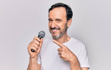 Orta yaşlı yakışıklı şarkıcı, izole edilmiş beyaz arka planda mikrofon kullanarak şarkı söylüyor.