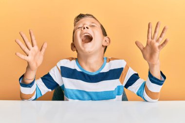 Kafkasyalı sevimli çocuk, gündelik giysiler içinde masada oturmuş başarıyı kutlarken kolları havada ve gözleri kapalı heyecanlı bir şekilde çığlık atıyordu. Kazanan konsept 