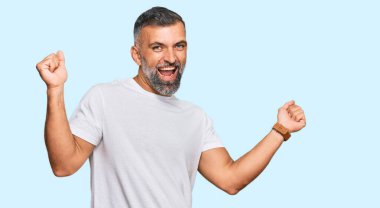 Orta yaşlı yakışıklı adam, gündelik beyaz tişört giyiyor mutlu ve neşeli dans ediyor, gülümsüyor rahat ve kendinden emin bir şekilde müzik dinliyor. 