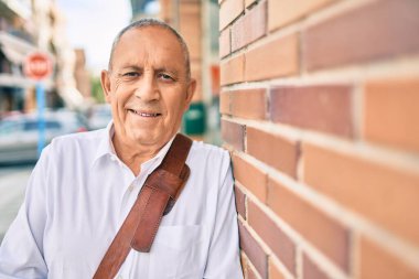 Kıdemli işadamı gülümsüyor. Şehrin duvarına yaslanıyor..