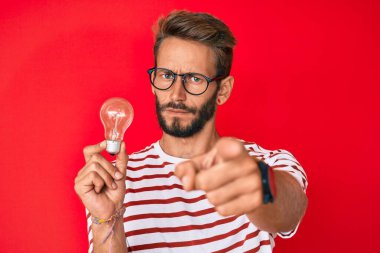 İlham ve fikir için elinde ampul tutan yakışıklı beyaz adam kamerayı ve seni işaret ediyor. Kendine güveni tam bir jest. 