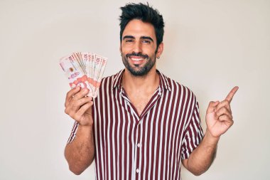 Yakışıklı, sakallı, Kolombiya pezosu tutan ve gülümseyen bir İspanyol. 