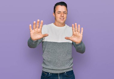 Kış süveteri giyen yakışıklı genç adam korku ifadesi yüzünden korkmuş ve dehşete düşmüş. El hareketlerini durdur, şok içinde bağır. panik konsepti. 